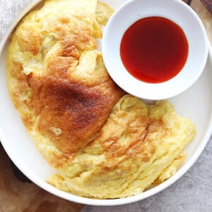 Fluffy Thai omelette served with a side of chili sauce.