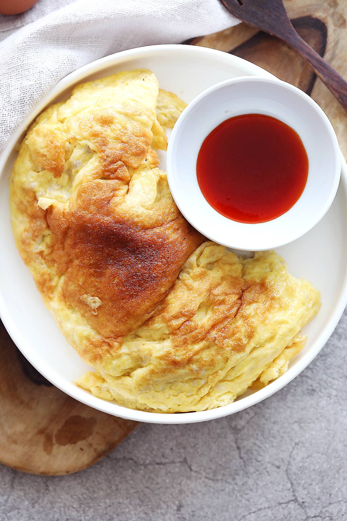 Fluffy Thai omelette served with a side of chili sauce.