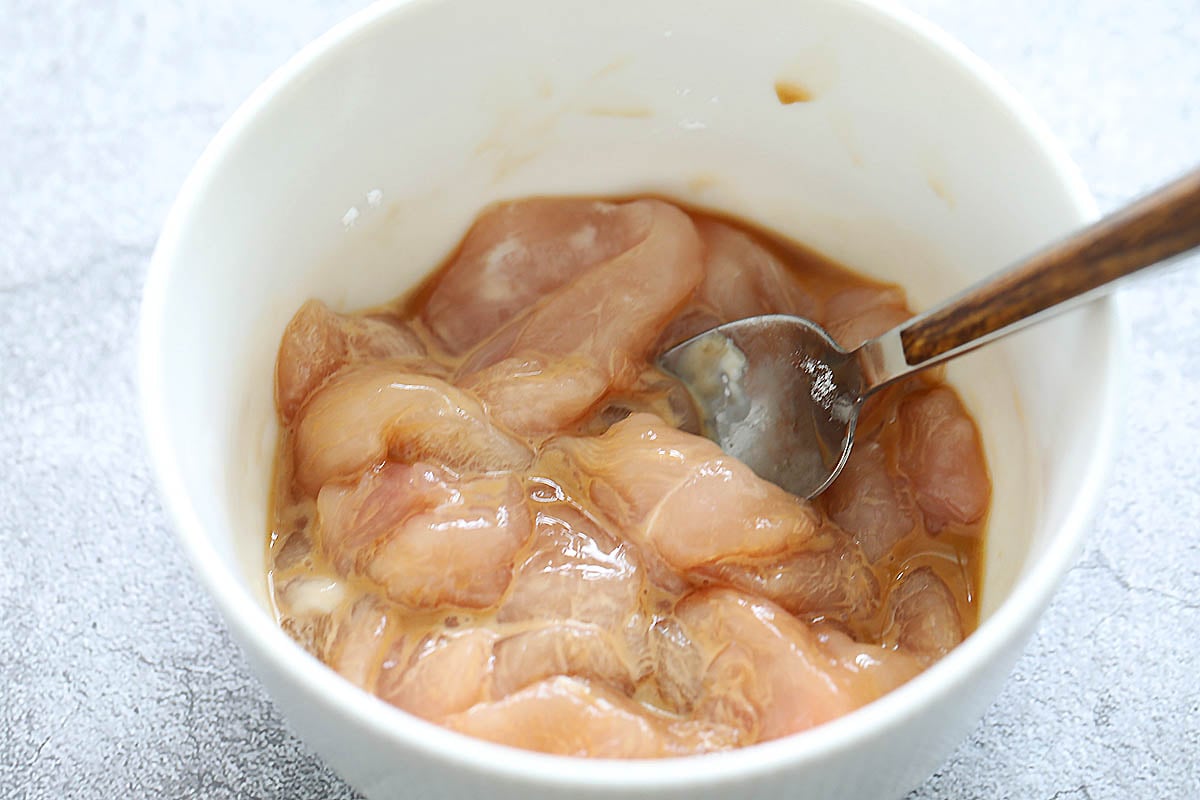 Chicken marinated with cornstarch and soy sauce in a bowl.