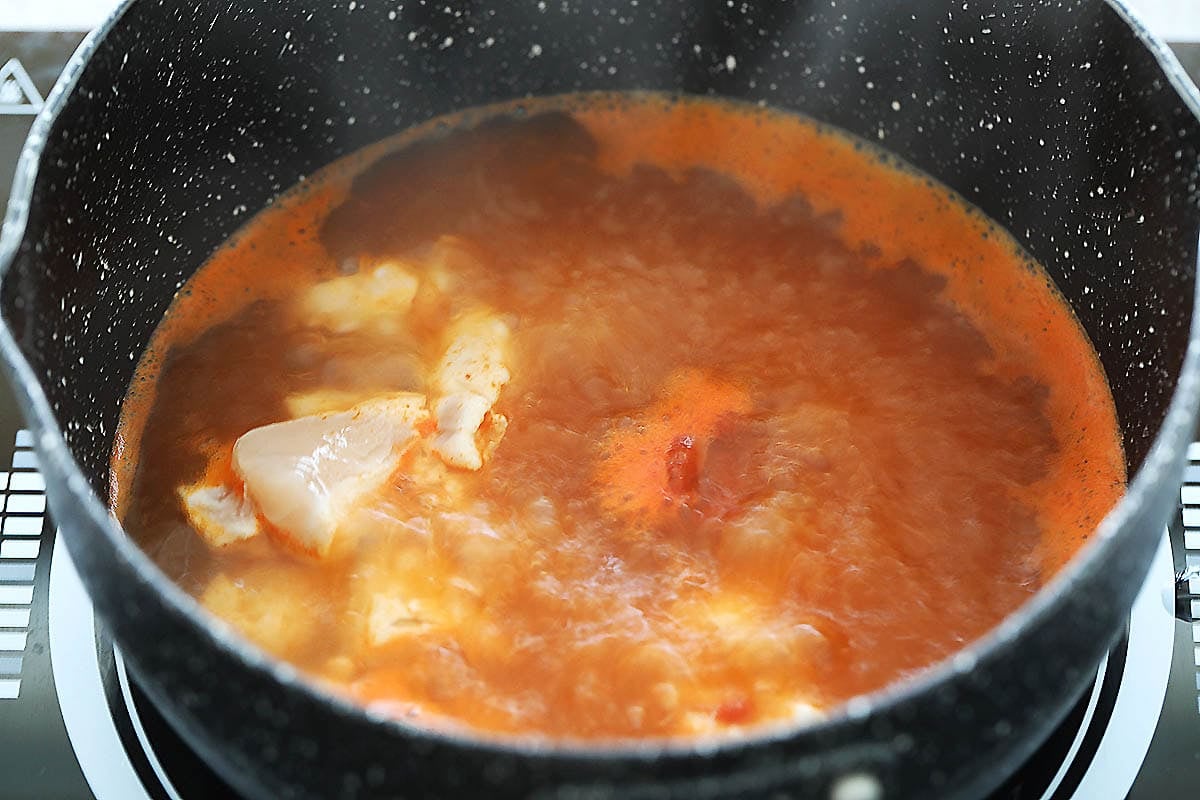 Chicken being boiled in Thai red curry broth.