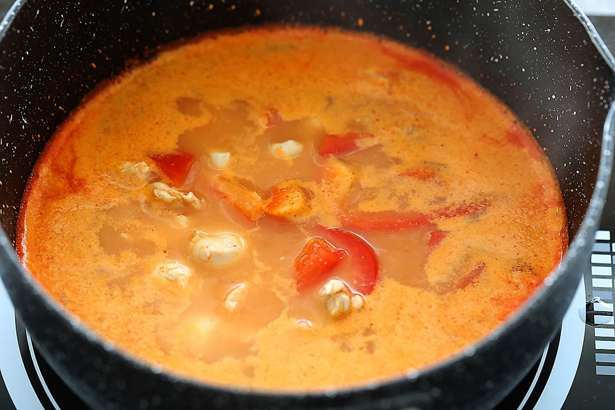 Thai coconut red curry broth with chicken and red bell pepper in a pot.