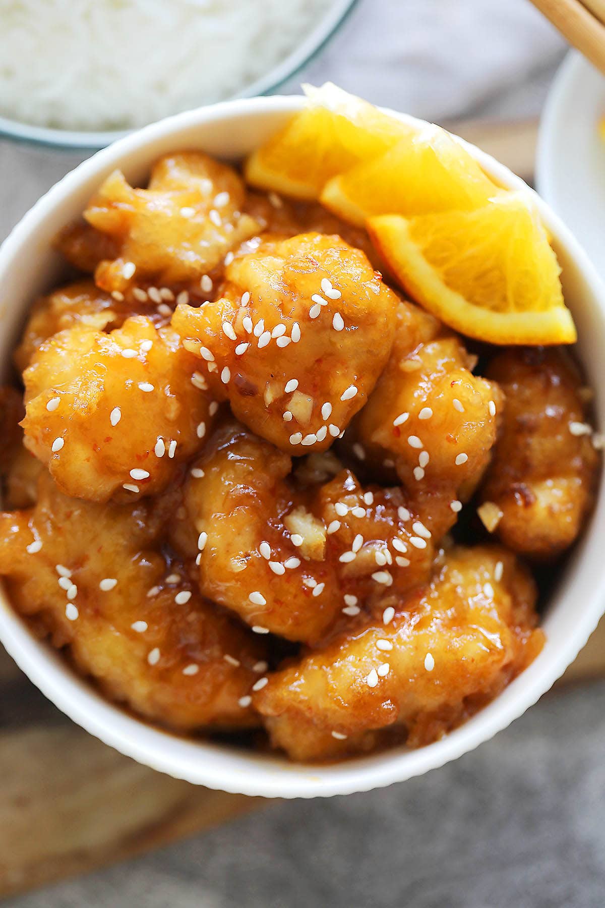 Orange chicken garnished with white sesame seeds and orange slices.