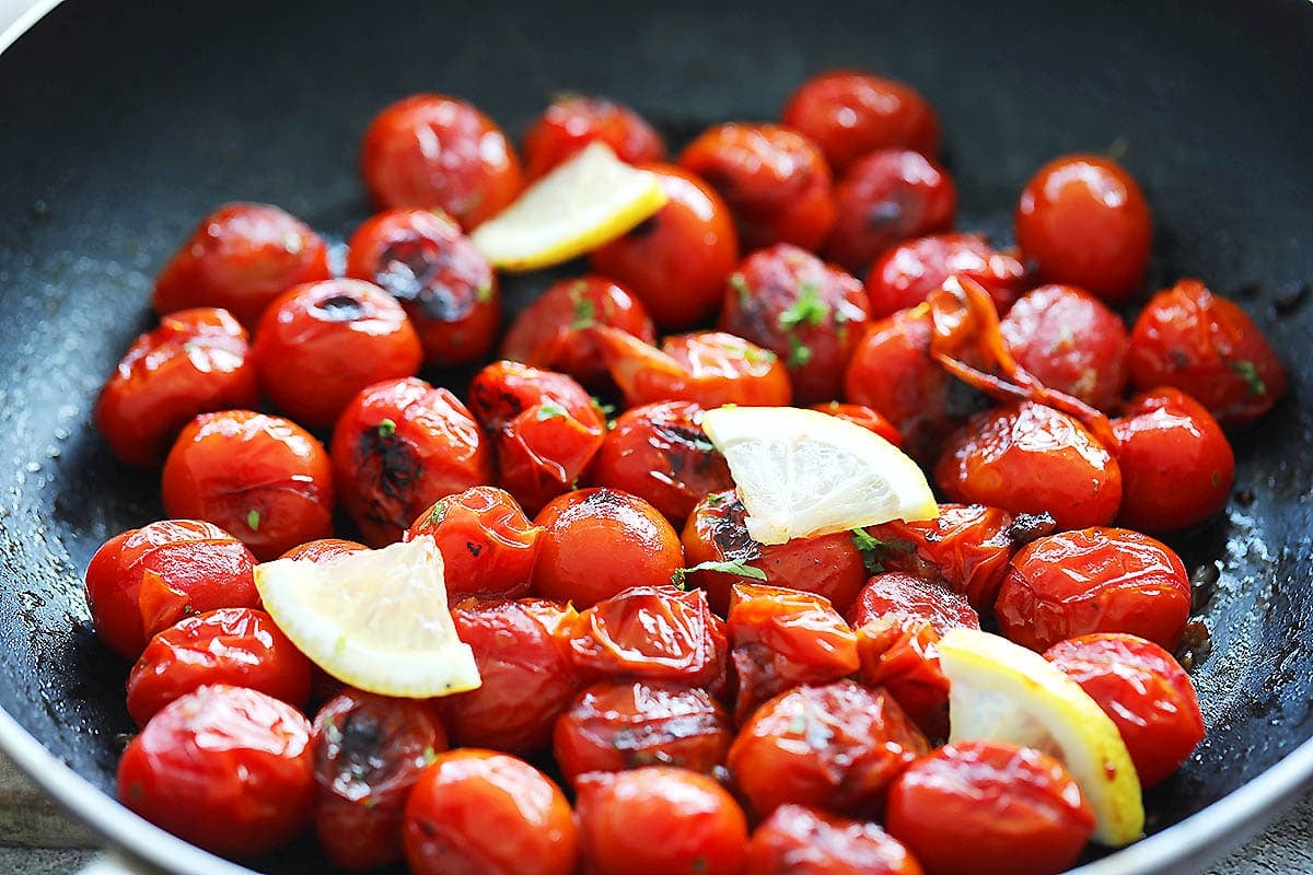 Grilled cherry tomatoes garnished with lemon slices in a pan.