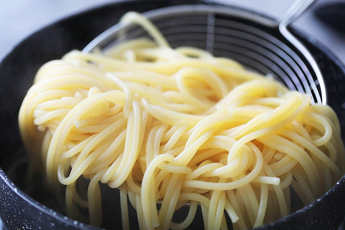 Cooked spaghetti on a strainer.