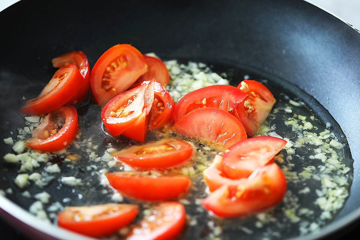 Chicken broth, garlic and tomatoes wedges in a pan.