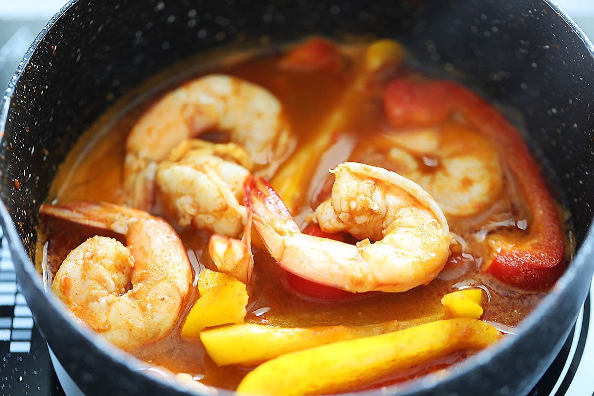 Shrimp, bell peppers, and water in a saucepan.