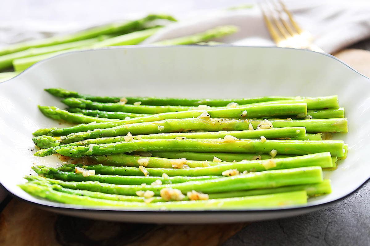 Pan sauteed asparagus with garlic and lemon juice served on a tray.