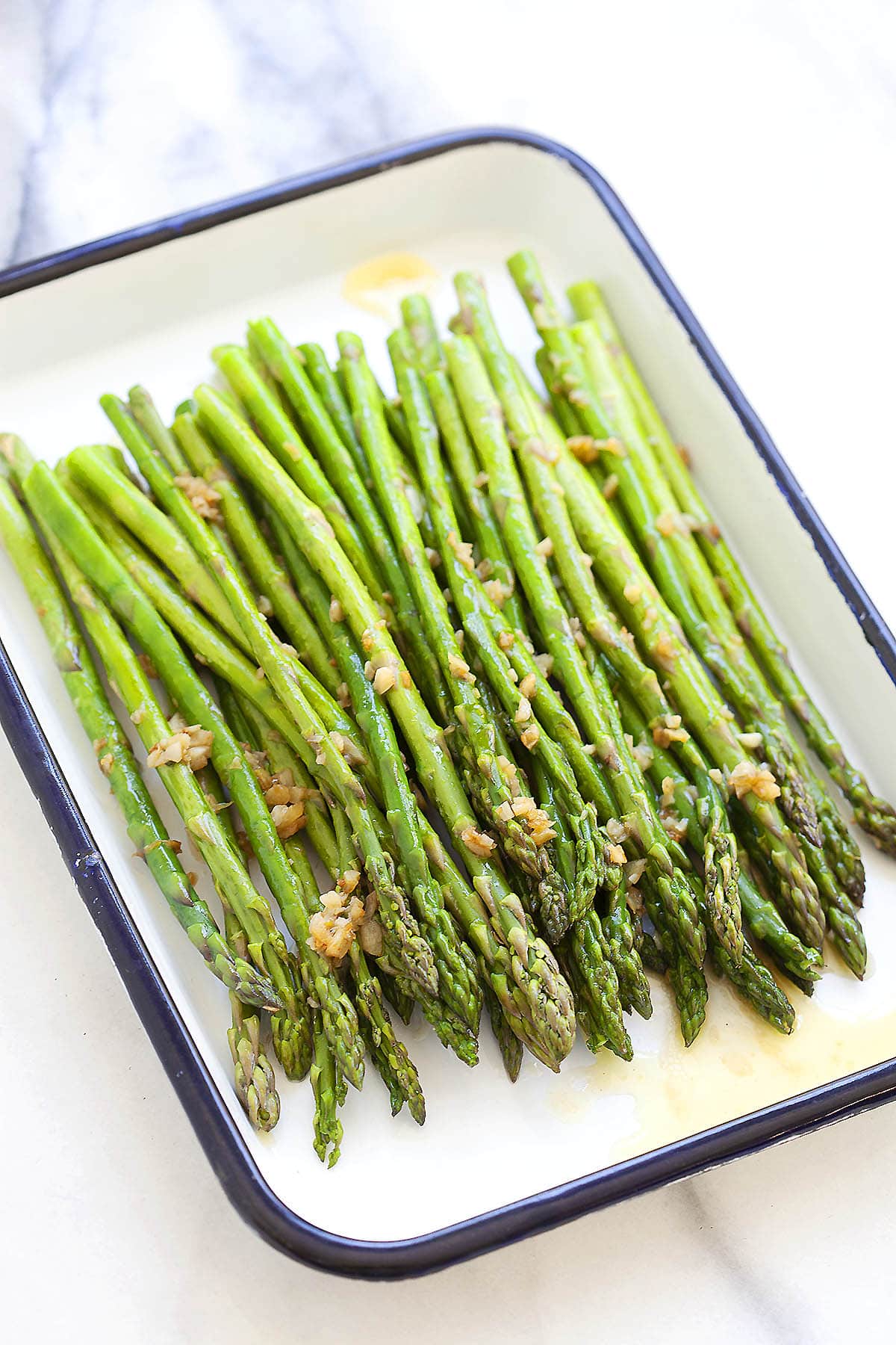 Sauteed asparagus with garlic butter served on a tray.
