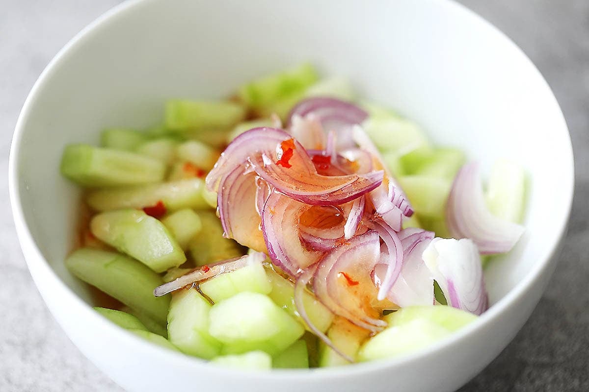 Cucumbers, Thai dressing and red onion in a bowl.