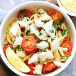 Crab pasta with cherry tomatoes and capers served with lemon wedges.