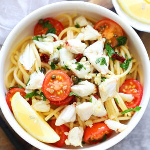 Crab pasta with cherry tomatoes and capers served with lemon wedges.