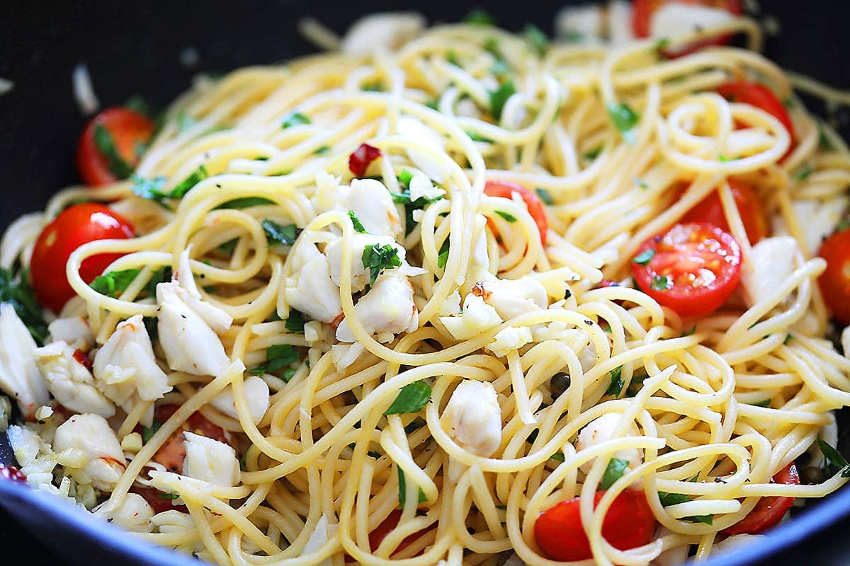Pasta with crab meat, cherry tomatoes, and parsley in a pan.