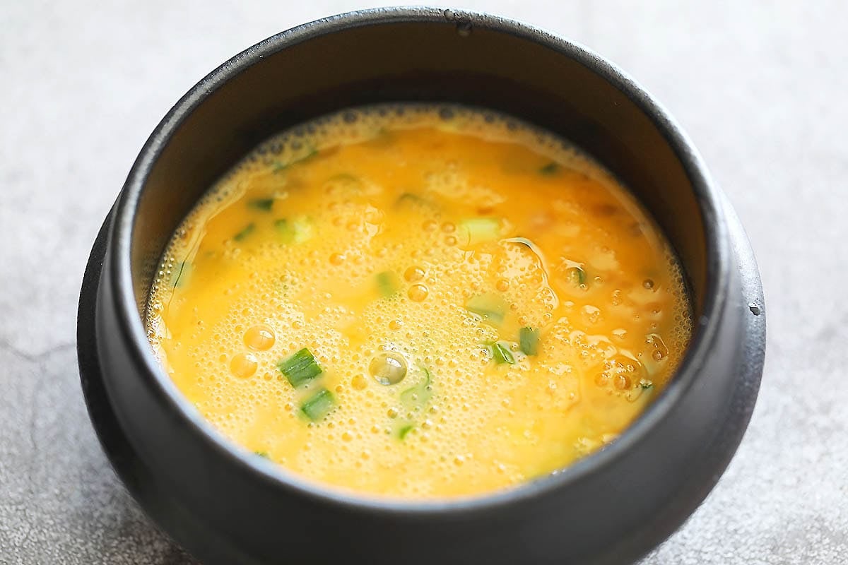 Beaten eggs and chopped scallions in an earthenware pot.