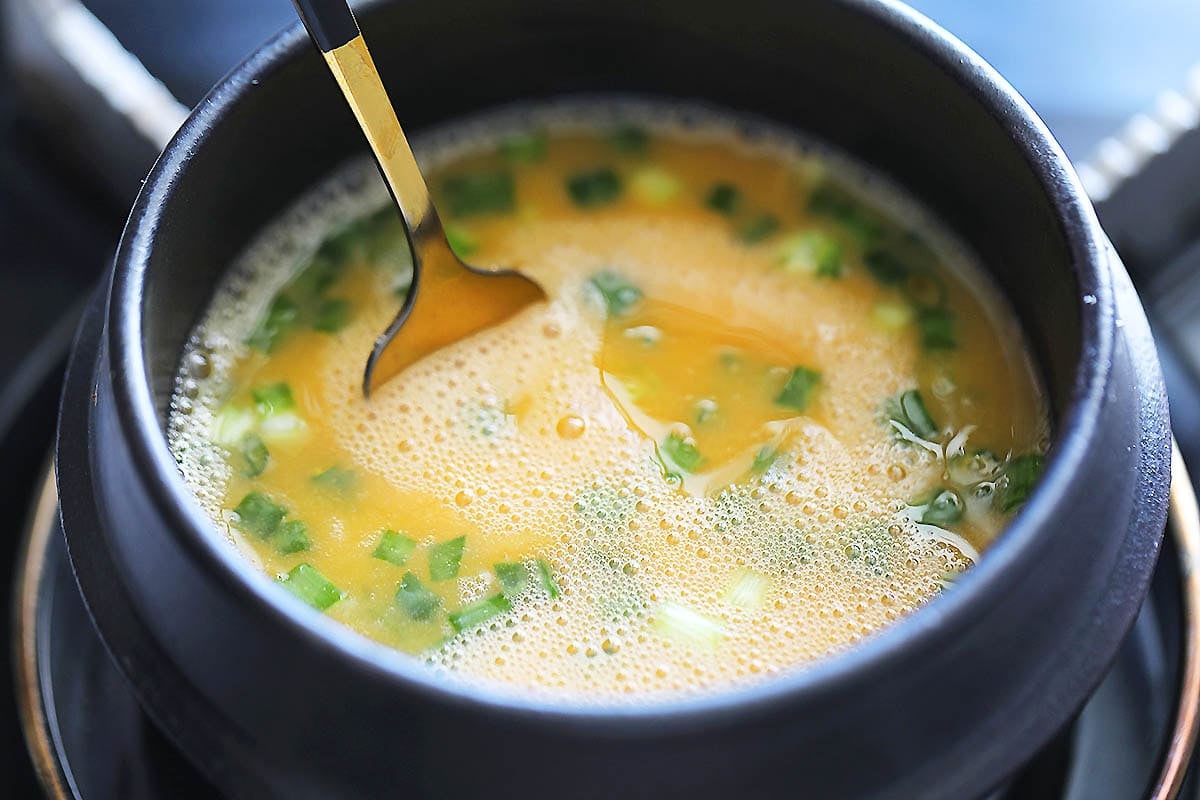 Fork in an earthenware pot with eggs and scallions.
