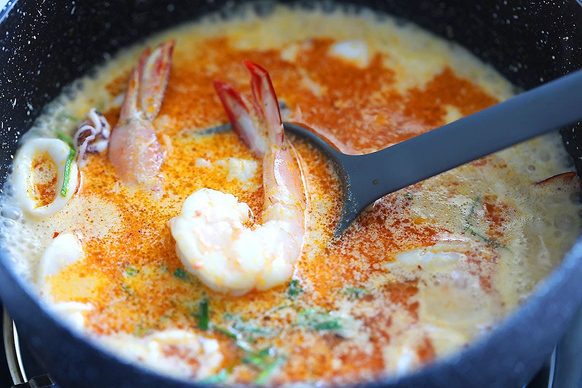 Creamy tom yum sauce for squid ink pasta with seafood in a saucepan.