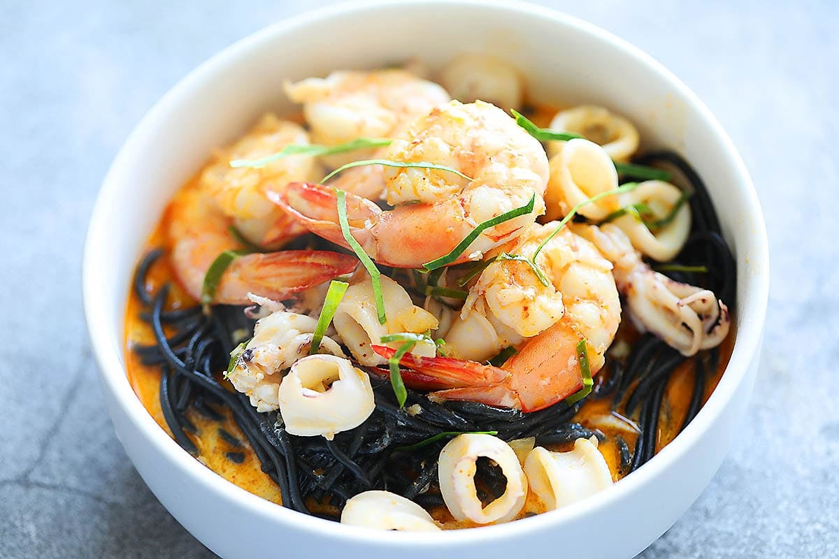 Seafood squid ink pasta with creamy tom yum sauce with kaffir lime leaves, served in a bowl.