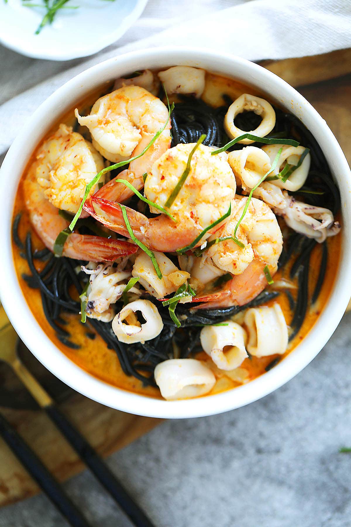 Creamy tom yum seafood squid ink pasta with shrimp and squid, served in a bowl.
