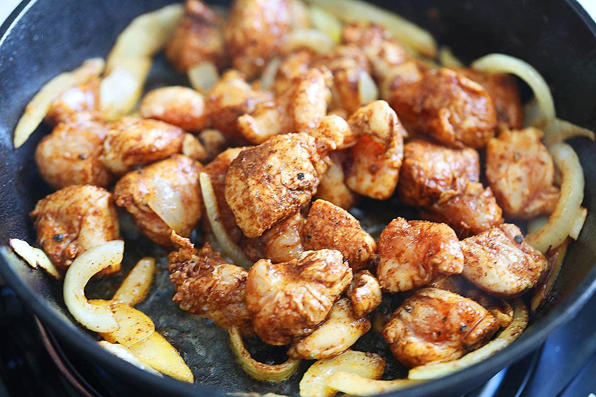 Chicken marinated with homemade fajita seasoning and onions in a cast iron skillet.