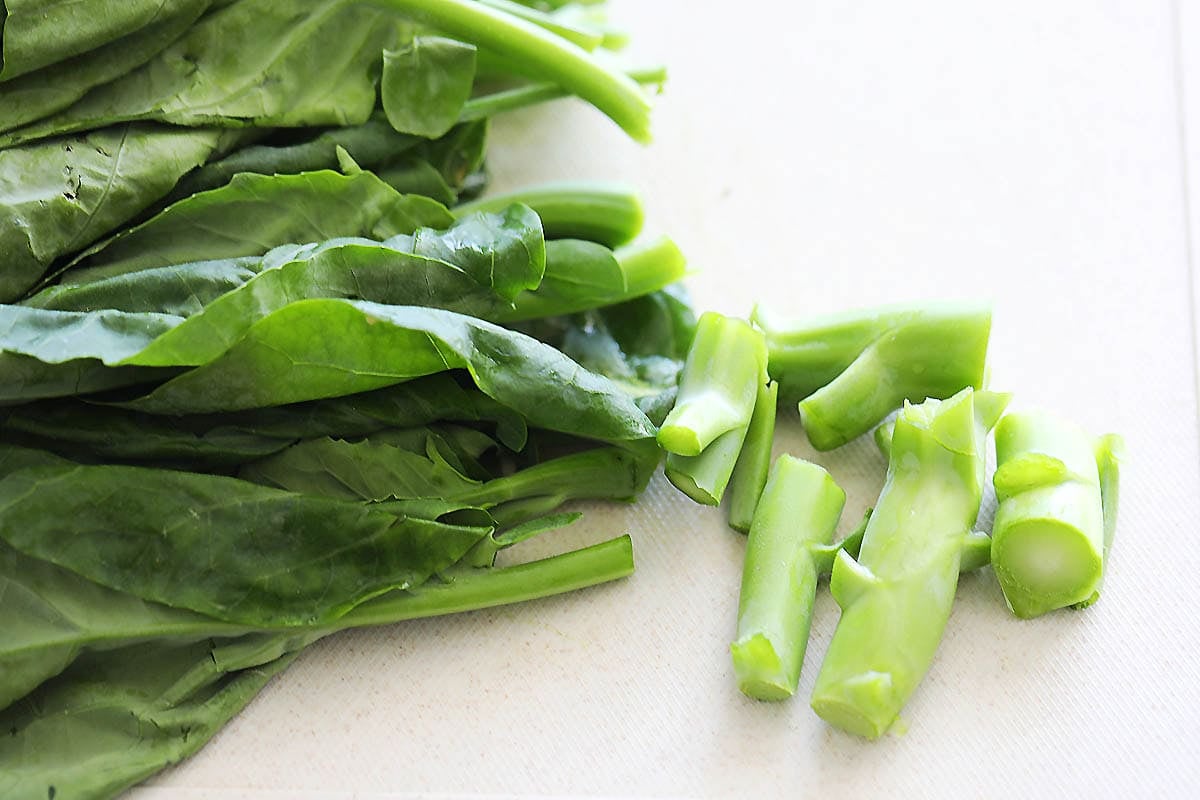 Chinese broccoli leaves and thick stems on a chopping board.