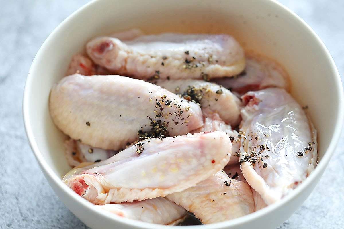 Chicken wings, black pepper, and lime juice in a bowl.