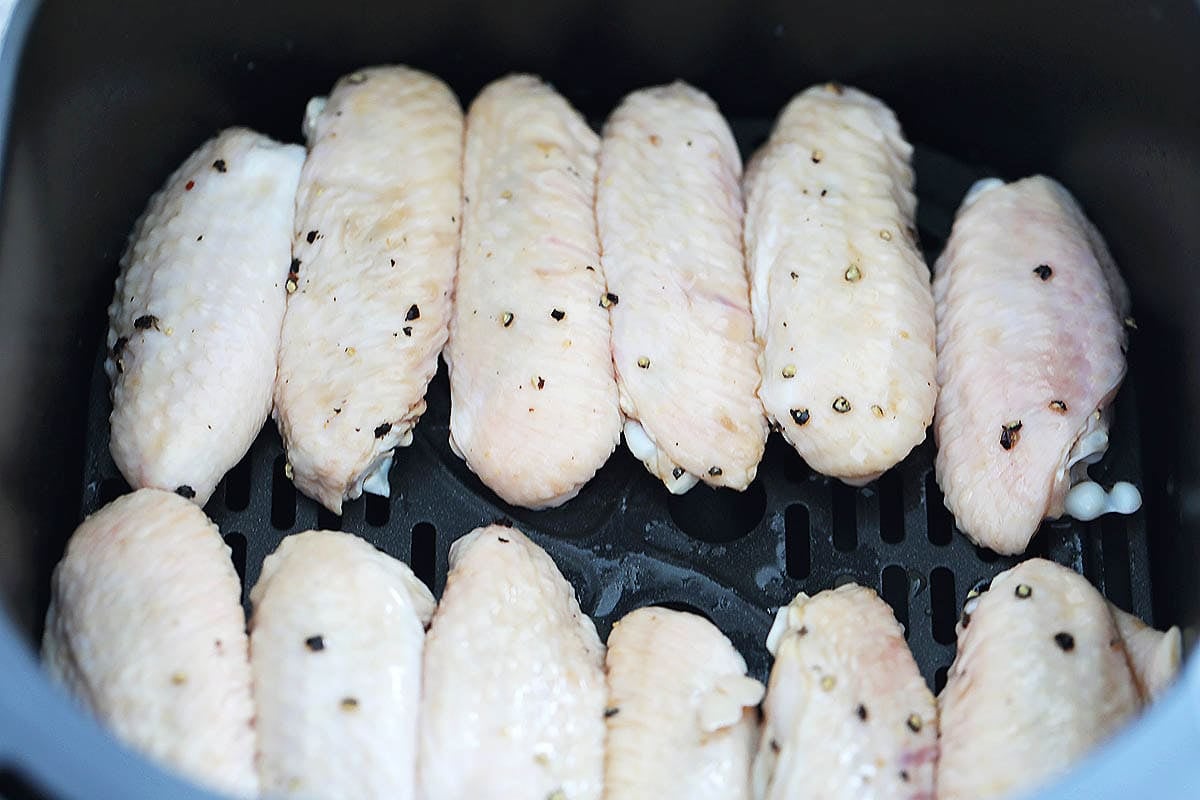 Marinated chicken wings in a single layer in an air fryer basket.
