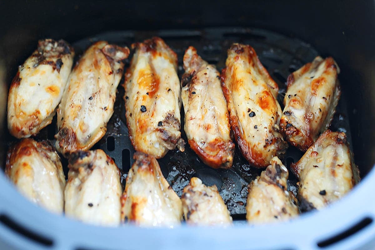Golden chicken wings in a single layer in an air fryer basket.