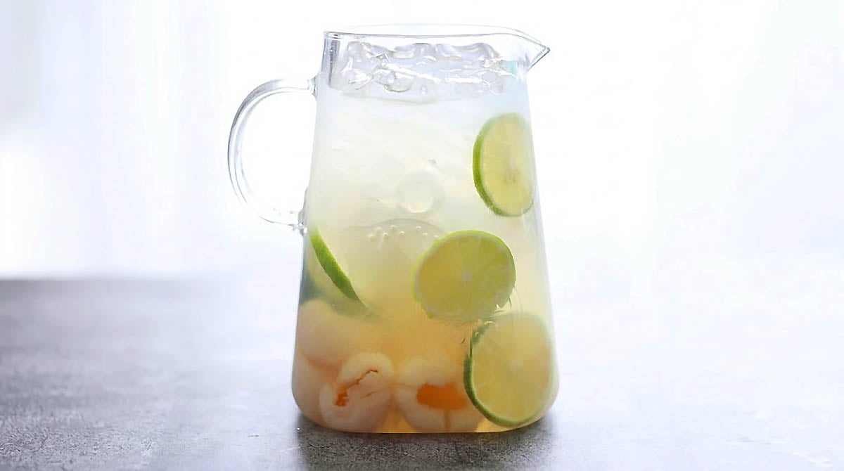 Lychee drink recipe with lime slices and lime juice in a pitcher.