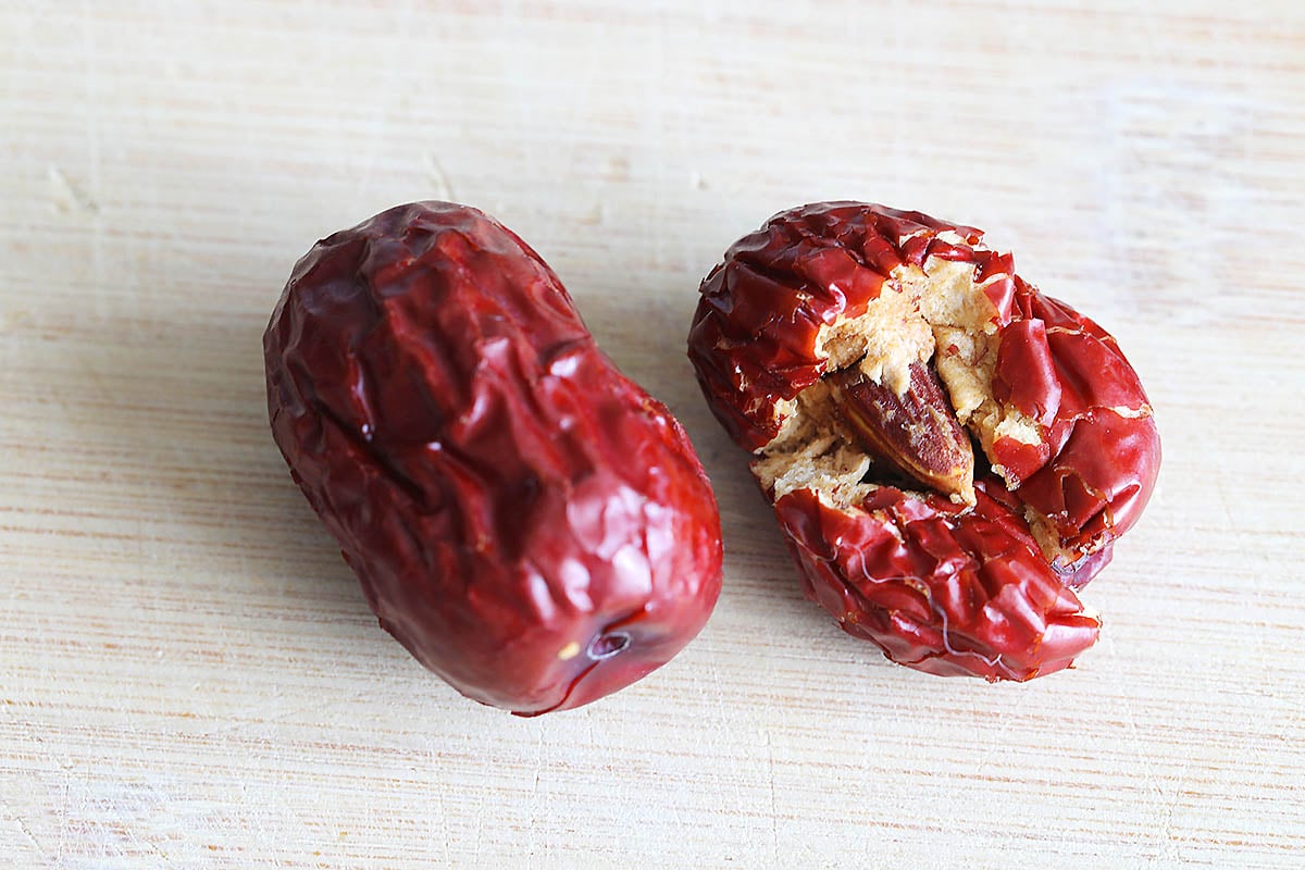 Red dates on a chopping board with one showing its seed.