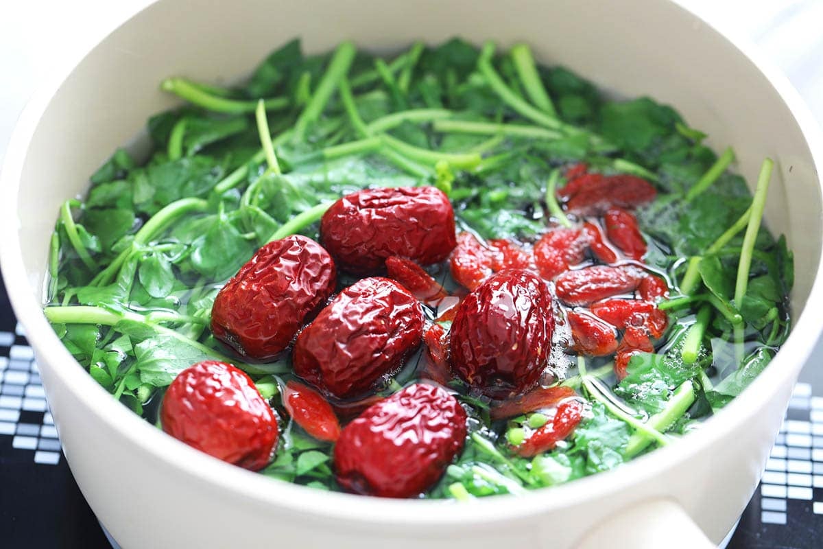 Watercress, red dates, and goji berries in a pot of water.