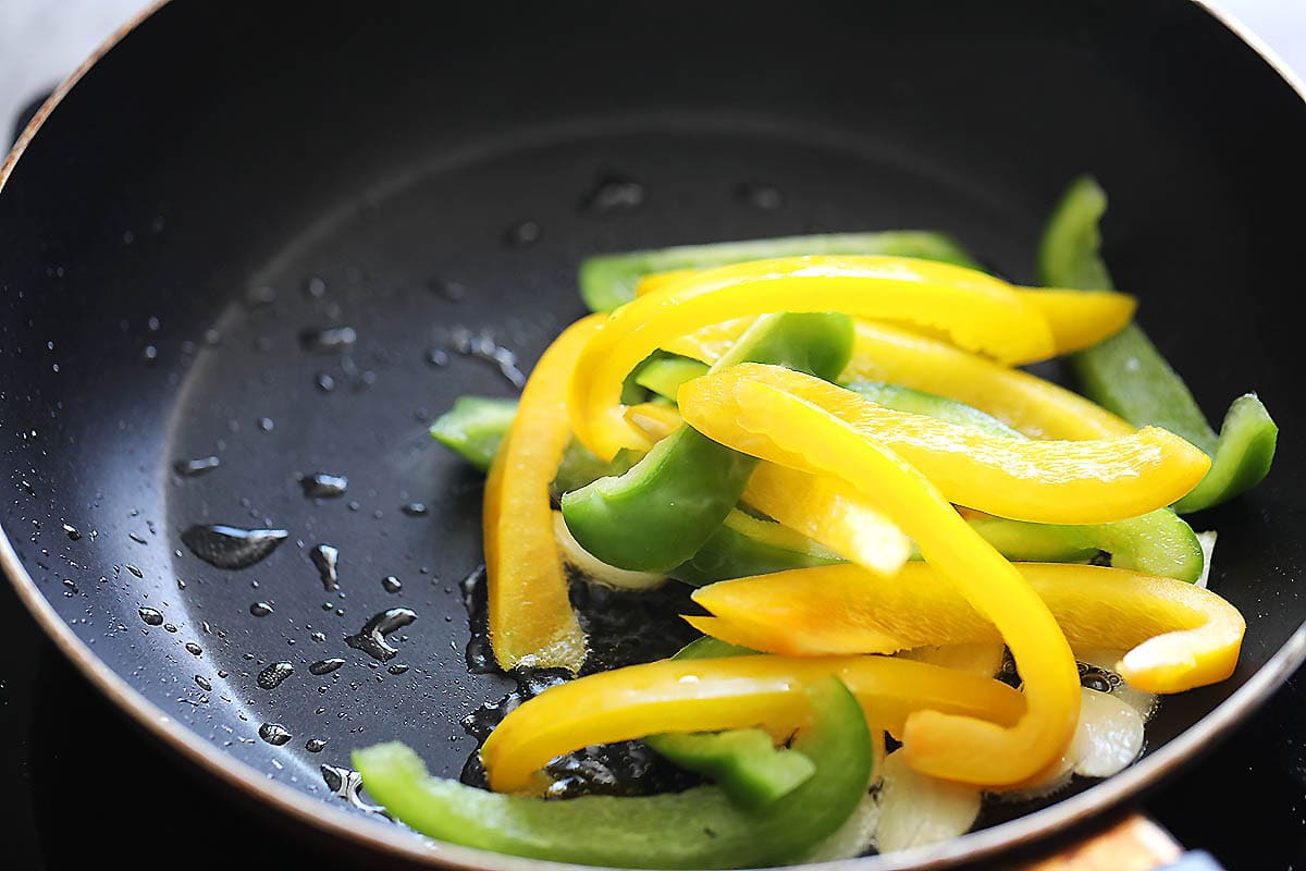 Green and yellow bell peppers, and garlic slices in a skillet.