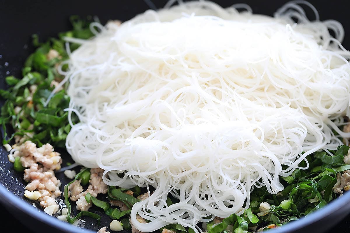 Ground pork, gai lan, and drained vermicelli in a pan.
