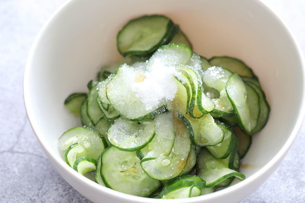 Cucumber slices, sugar, sesame oil, and rice vinegar in a bowl.