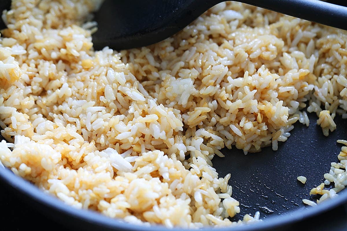 Rice evenly coated with soy sauce and fish sauce in a pan.