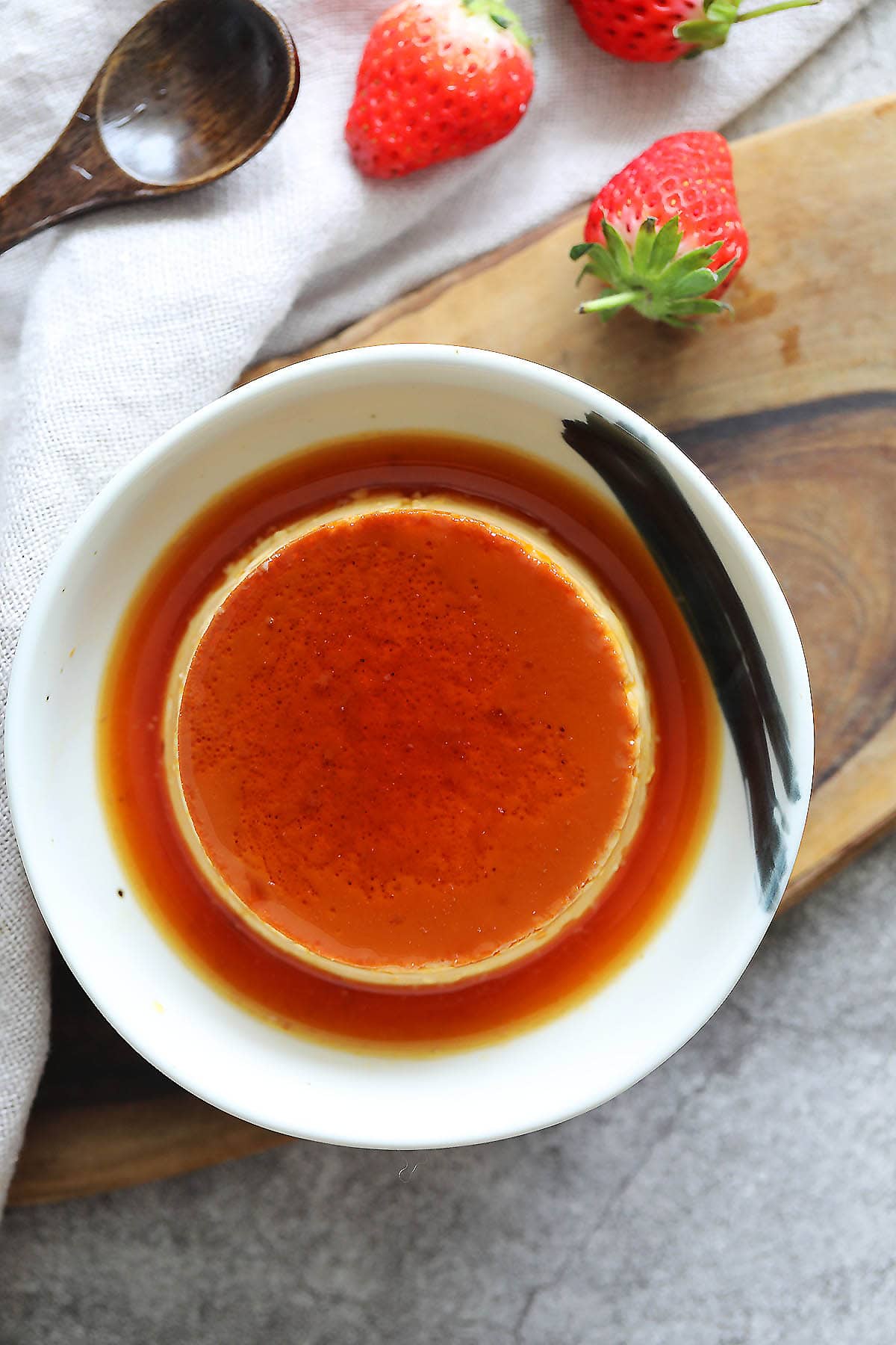 French creme caramel recipe served in a shallow bowl with strawberries.