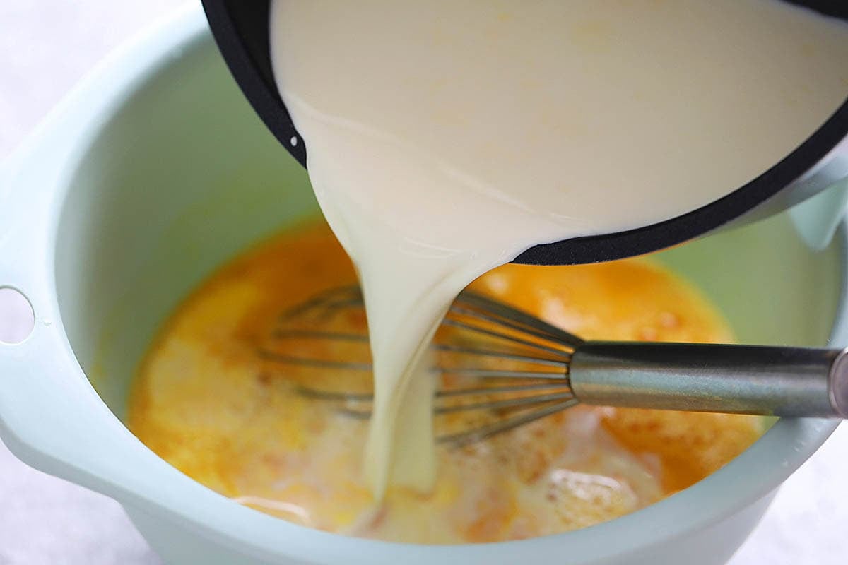 Warm milk being poured into a large bowl with eggs.
