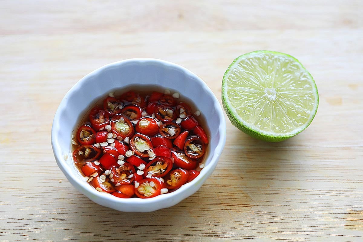 Prik nam pla with half a lime on a chopping board.