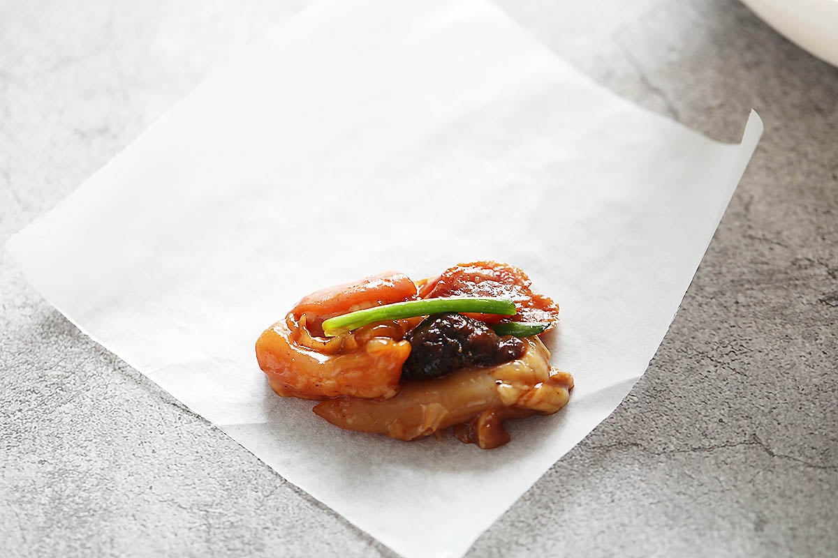 Marinated chicken, Chinese sausage, mushroom, and scallion on a piece of square parchment paper.