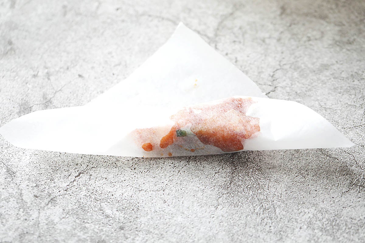 Bottom part of the square parchment paper with the chicken rolled upwards.