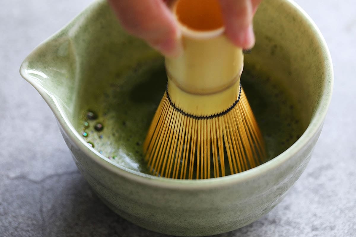 Bamboo whisk whisking matcha in a chawan.