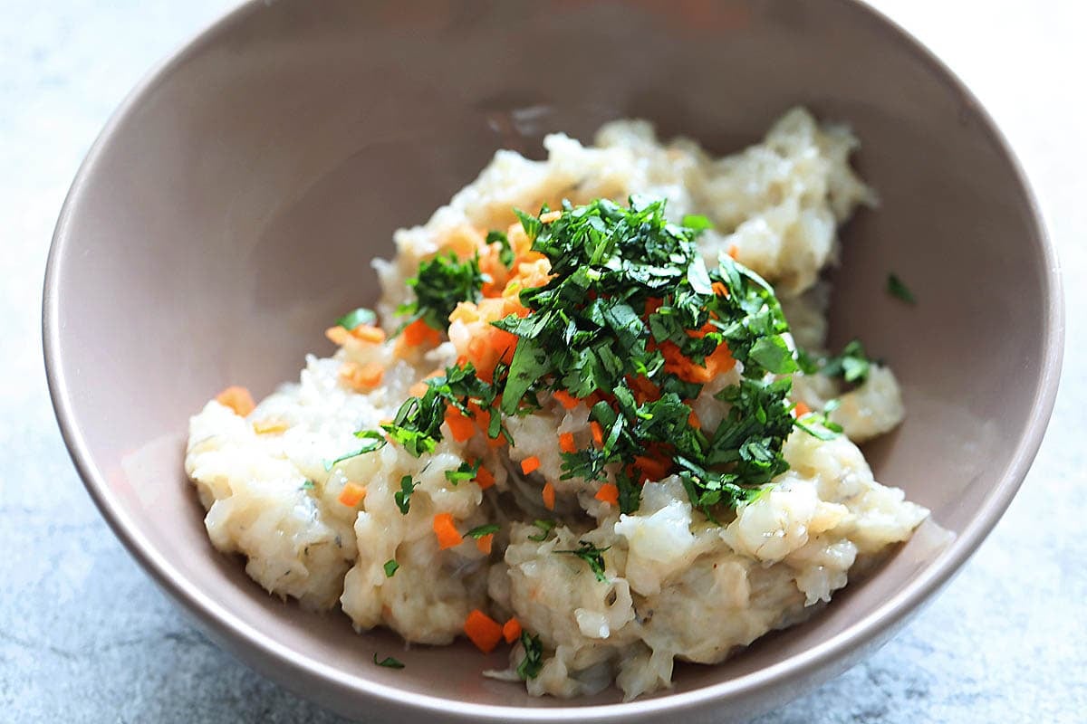 Shrimp mousse, cilantro leaves and diced carrots in a bowl.