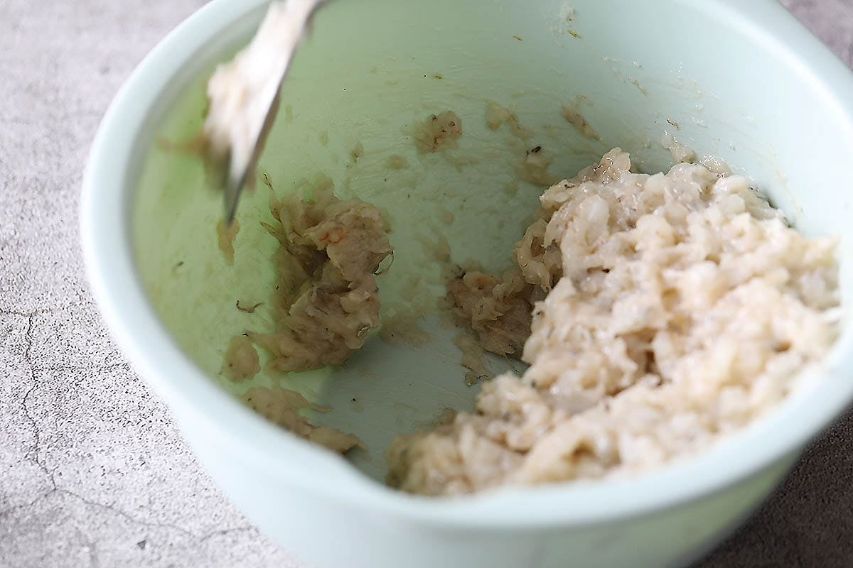 A spoonful of shrimp mixture being thrown into a bowl.