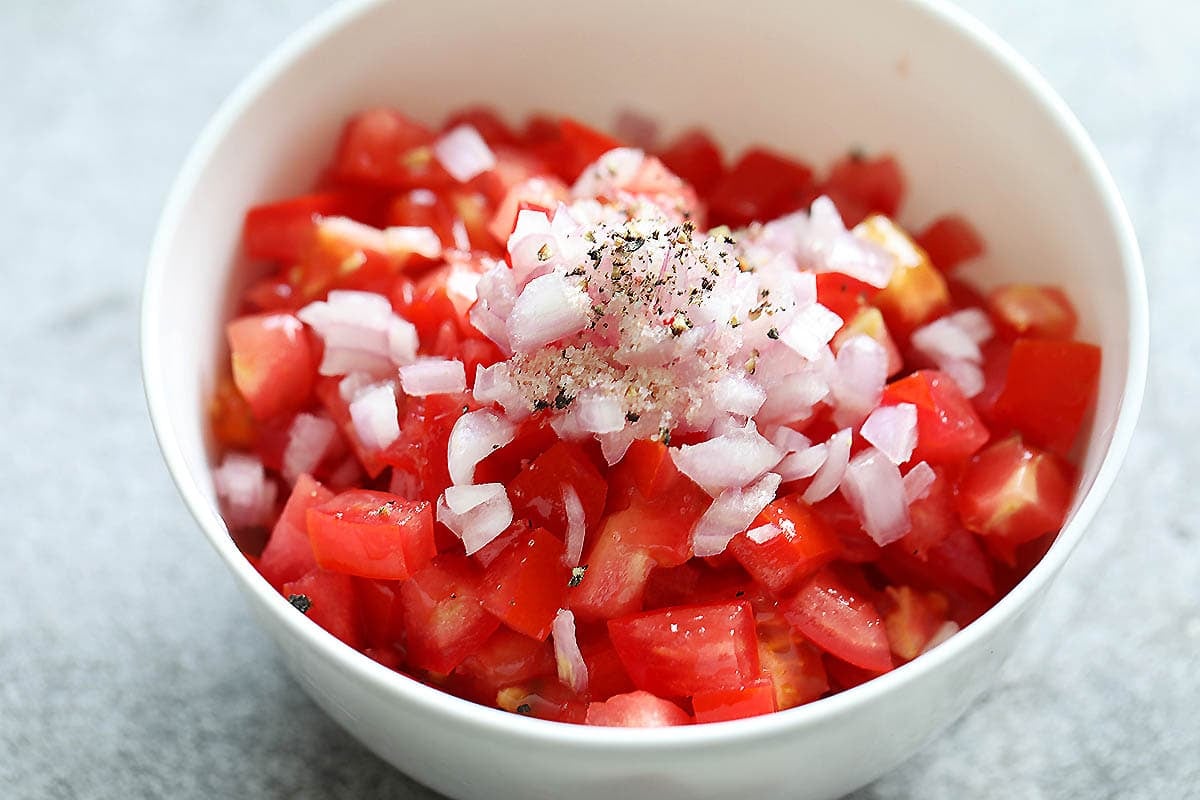 Cubes tomatoes, diced red onions, and seasoning in a bowl.