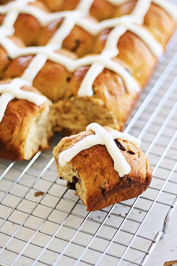 Easy soft, fluff and pillowy hot cross buns spiced with cinnamon, cloves and loaded with dried fruits, on a cooling rack.